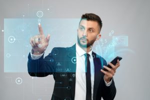 Front view of businessman in suit holding phone with virtual projection in office. Serious bearded man clicking virtual button on digital tactile charts screen. Concept of gadgets, digitalization.