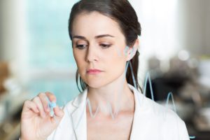 Closeup of sad pretty businesswoman drawing graph on transparent glass and standing behind it with blurry office interior in background